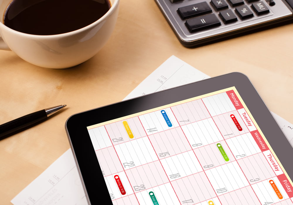 Workplace with tablet pc showing calendar and a cup of coffee on a wooden work table close-up-1
